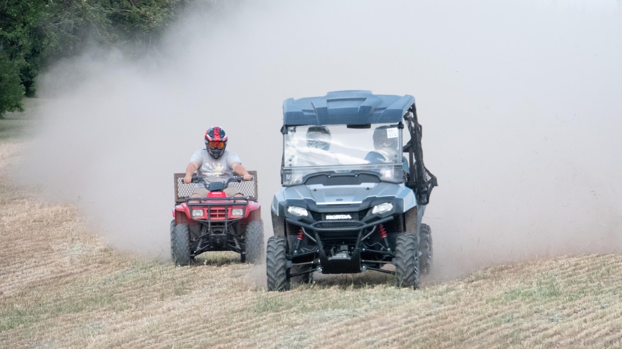 Deux VTT conduits par des gens portant des casques circulent à travers un champ agricole en faisant de la fumée et de la poussière.