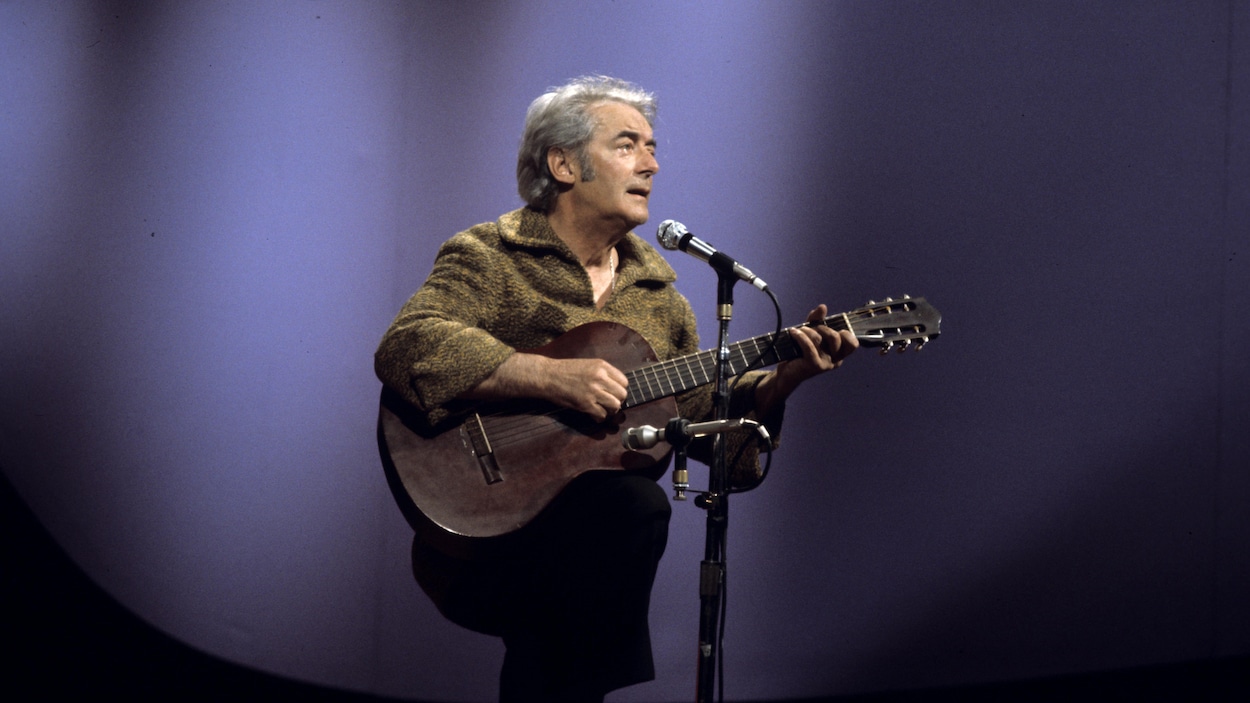 Dans un studio de télévision, le chanteur
Félix Leclerc, chante en s'accompagnant de
sa guitare devant un micro sur pied Dans un studio de télévision, le chanteur
Félix Leclerc, chante en s'accompagnant de
sa guitare devant un micro sur pied