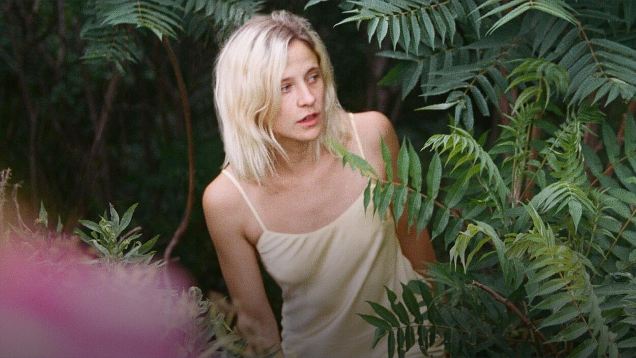 La chanteuse est entourée de végétation tropicale.