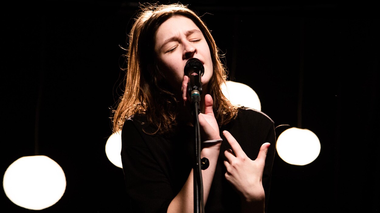 La jeune artiste Lou-Adriane Cassidy chante, avec émotions et les yeux fermés, sa chanson Poussière dans les studios de Radio-Canada.