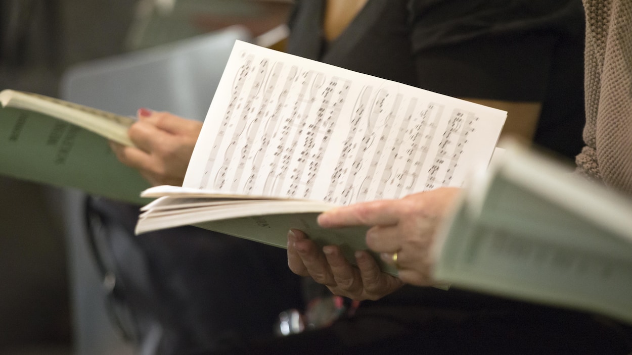 Gros plan sur des mains de membres d'une chorale tenant des livrets de chants