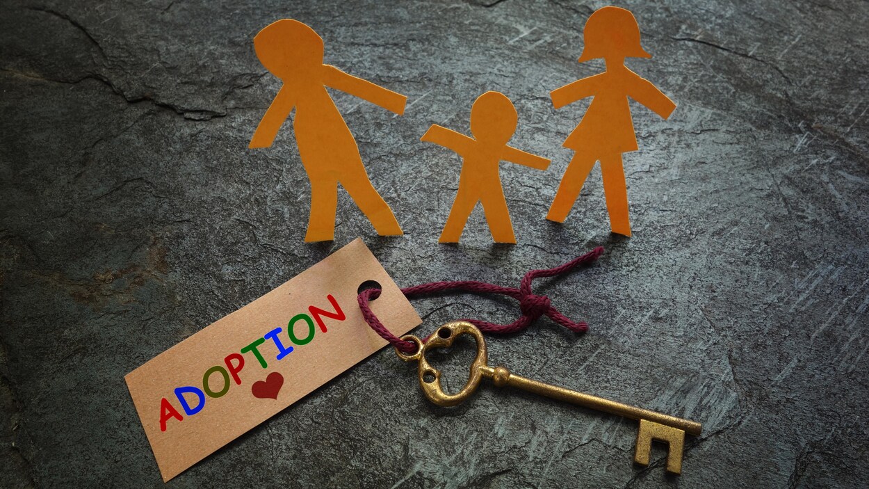 Représentation d'une famille en figurines de papier, placées tout près d'une clé de maison familiale et d'une étiquette portant la mention Adoption.