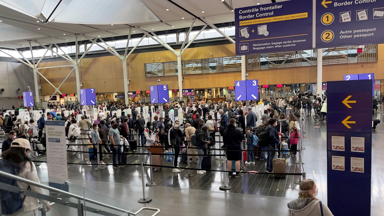 Des gens font la file avec leurs bagages pour passer le contrôle frontalier à l'Aéroport international Pierre-Elliott-Trudeau de Montréal. 