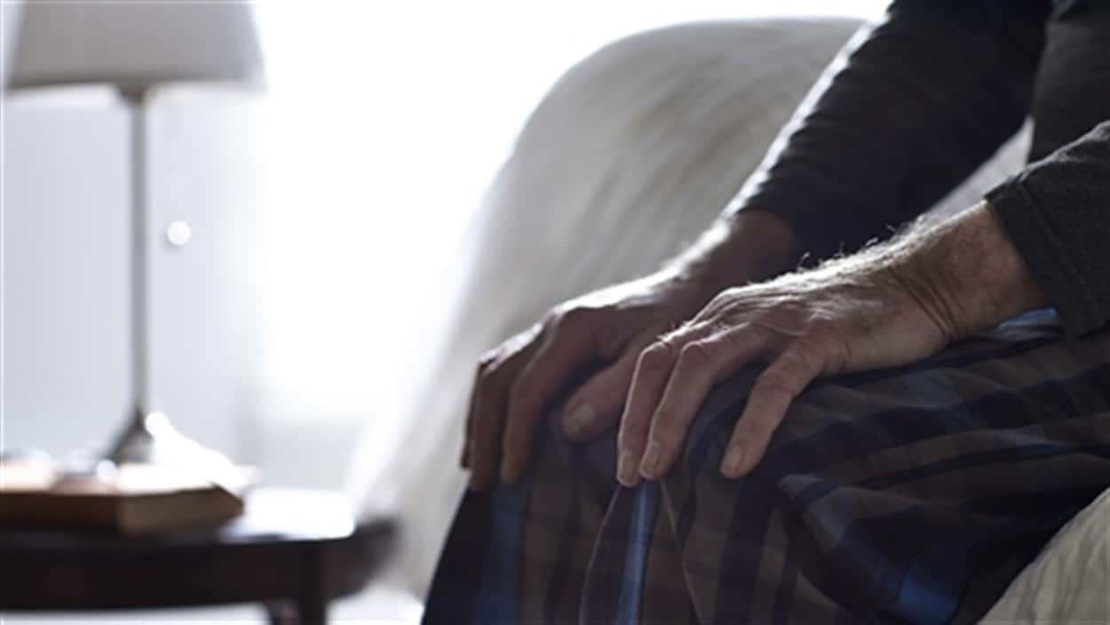 Les mains d'un homme âgé assis sur son lit.
