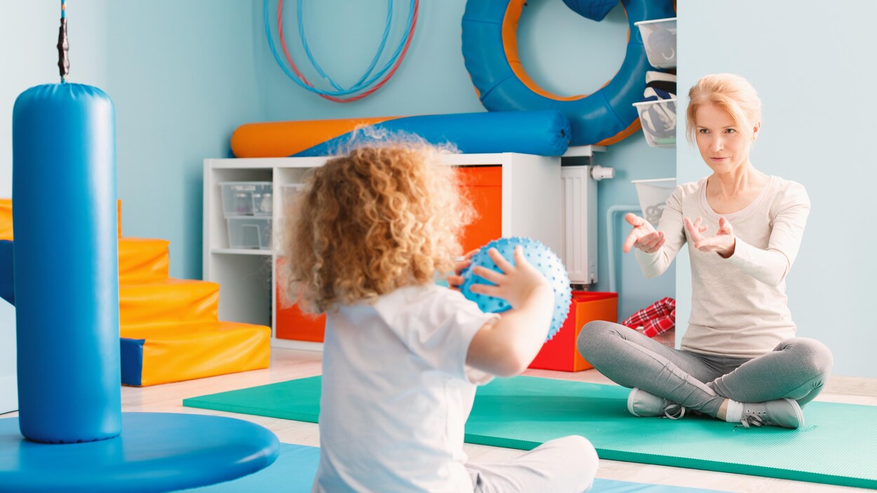 Un enfant autiste et sa thérapeute, jouant au ballon.