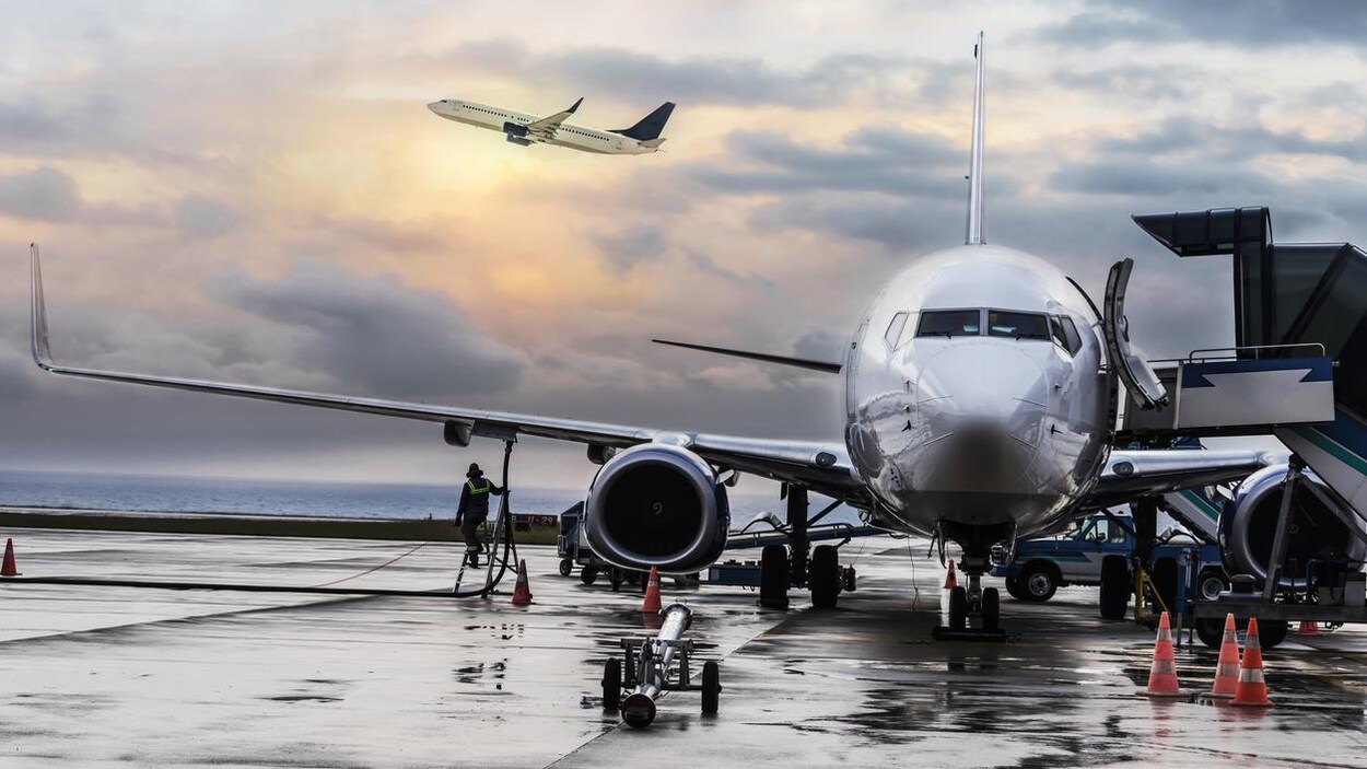 Un avion est sur le tarmac d'un aéroport pendant qu'un autre décolle.
