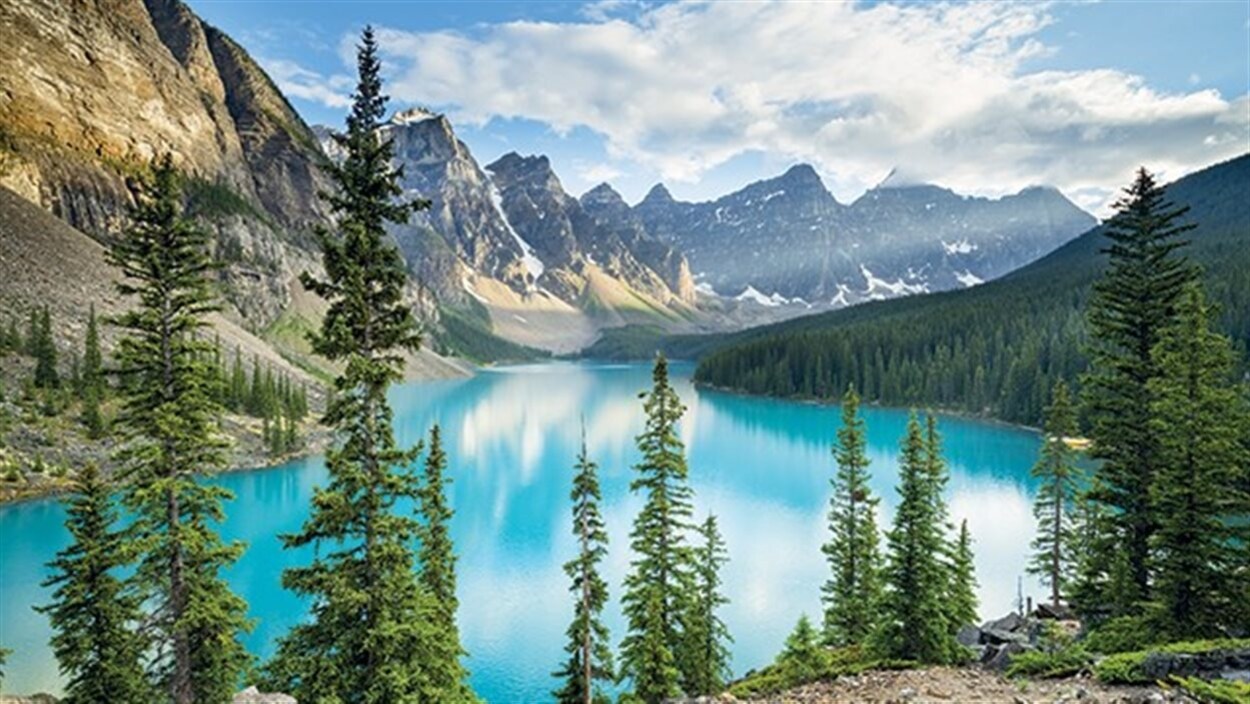 Des montagnes entourent un lac sur rives duquel poussent des conifères.