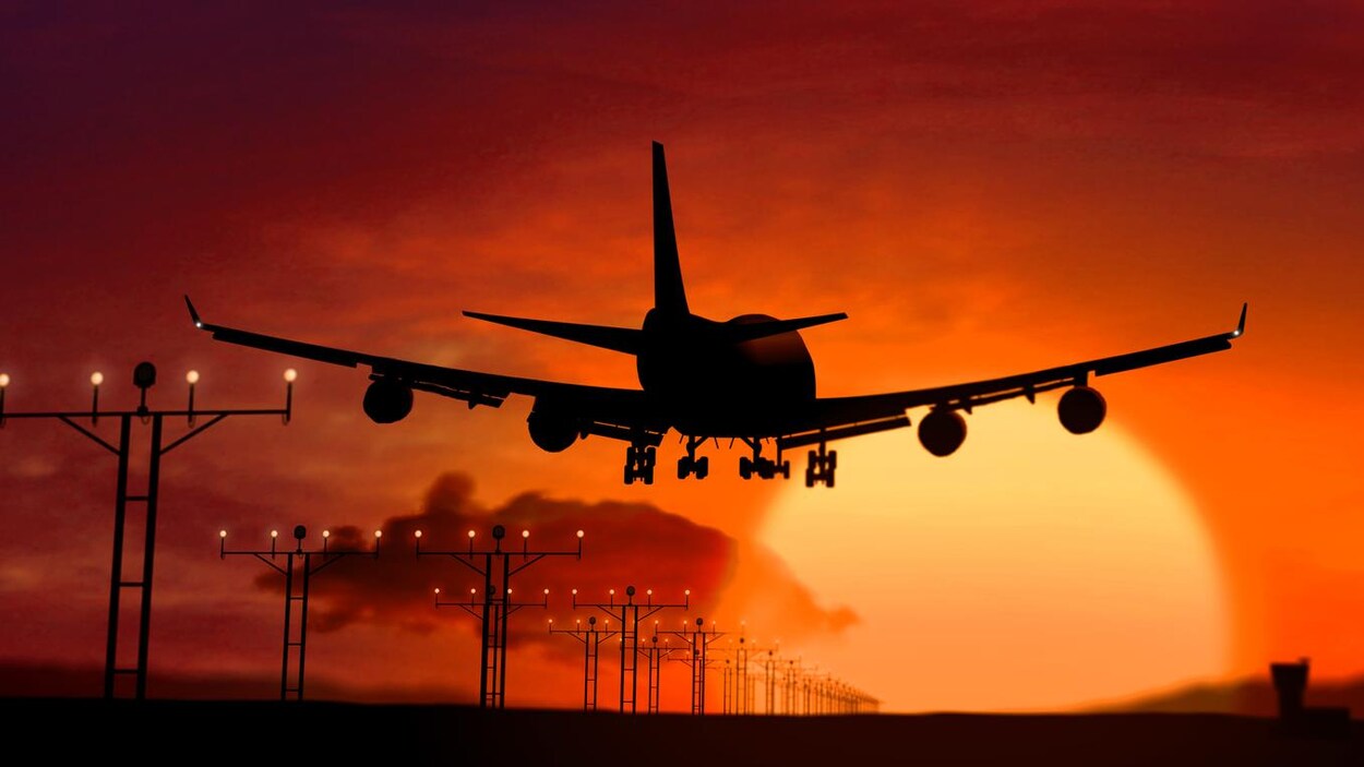 Silhouette d’avion atterrissant sur coucher de soleil.