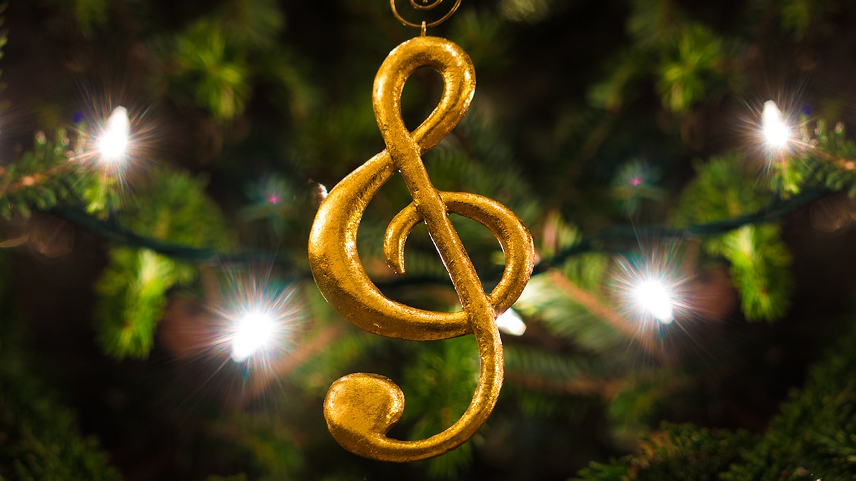Un ornement en forme de clé de sol devant des branches de sapin et des lumières de Noël