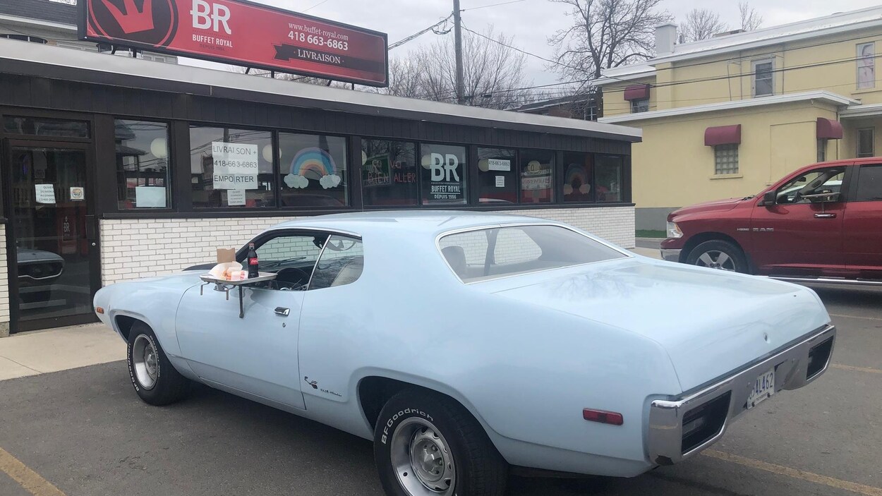 Une voiture ancienne est stationnée devant le restaurant Buffet Royal avec à la fenêtre un plateau pour le service au volant.