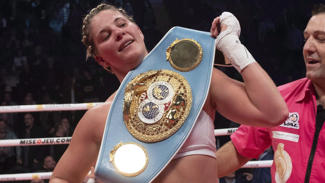 Elle est dans un ring et tient une grande ceinture ornementée d'écussons et de dorures.