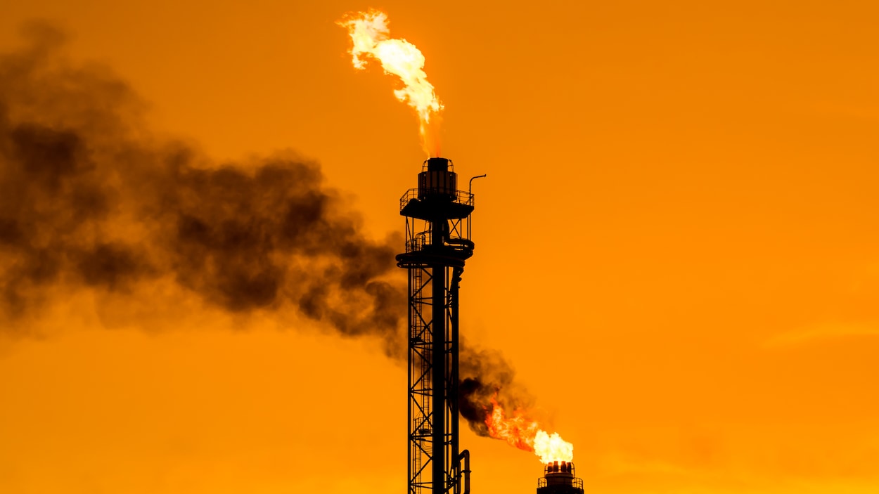 Des flammes brûlent au sommet de deux cheminées, dans une raffinerie de pétrole.