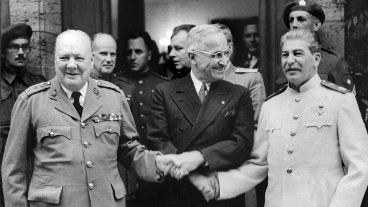 Photo d'archives sur les marches d'un édifice. Les trois dirigeants sourient et se serrent la mai.