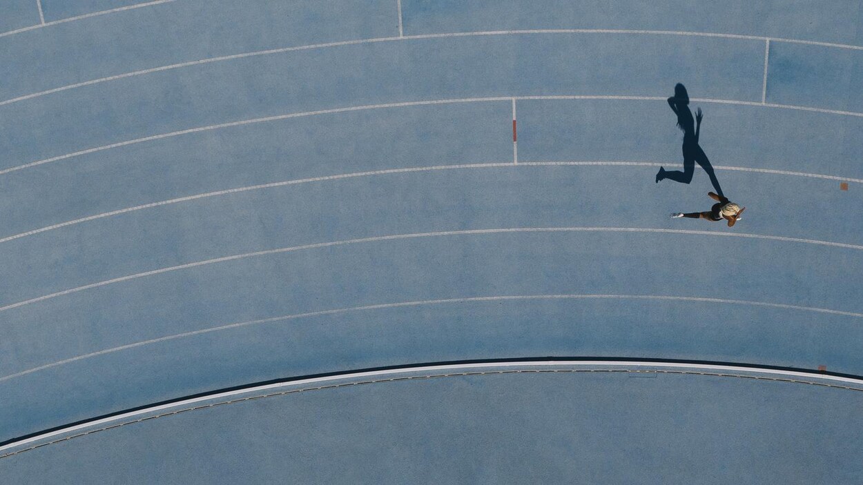 Une coureuse et son ombre vues de haut sur une piste bleue.