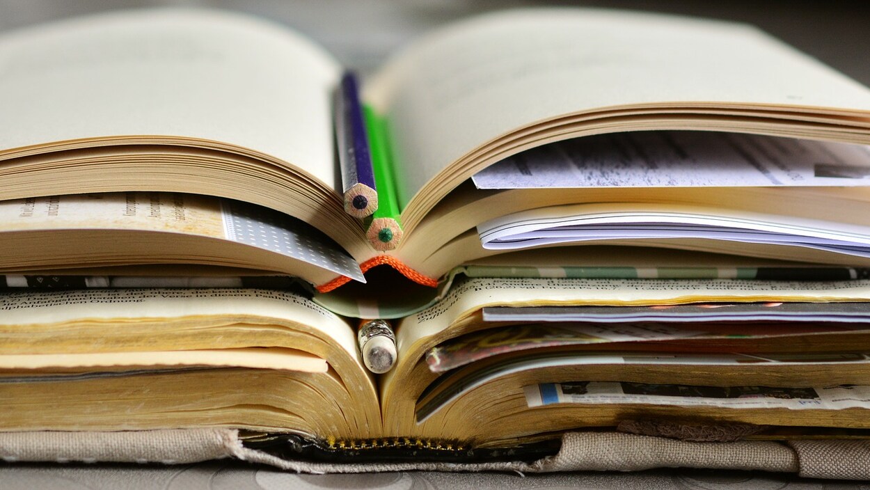 Gros plan de livres ouverts empilés avec des crayons et des feuilles glissées à l'intérieur de ceux-ci.