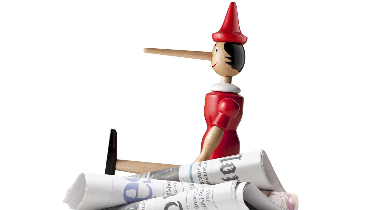 Un Pinocchio assis sur une pile de journaux pour représenté les Fake News.