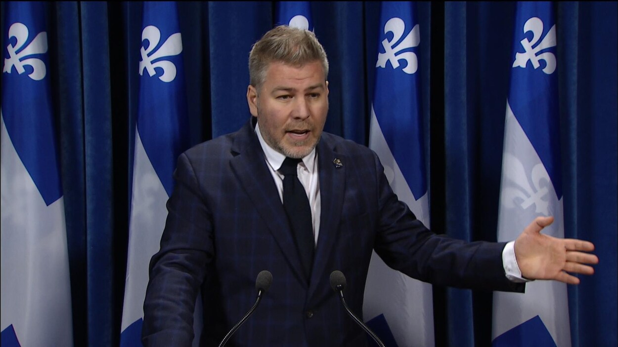 Pascal Bérubé parle, debout en costume bleu carreauté, main gauche en l'air.
