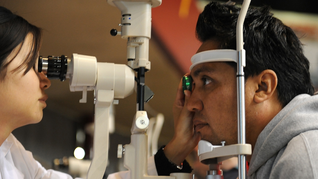 Une optométriste réalise un examen de la vue sur un homme dont le menton et le front sont appuyés contre un instrument pour stabiliser son visage.