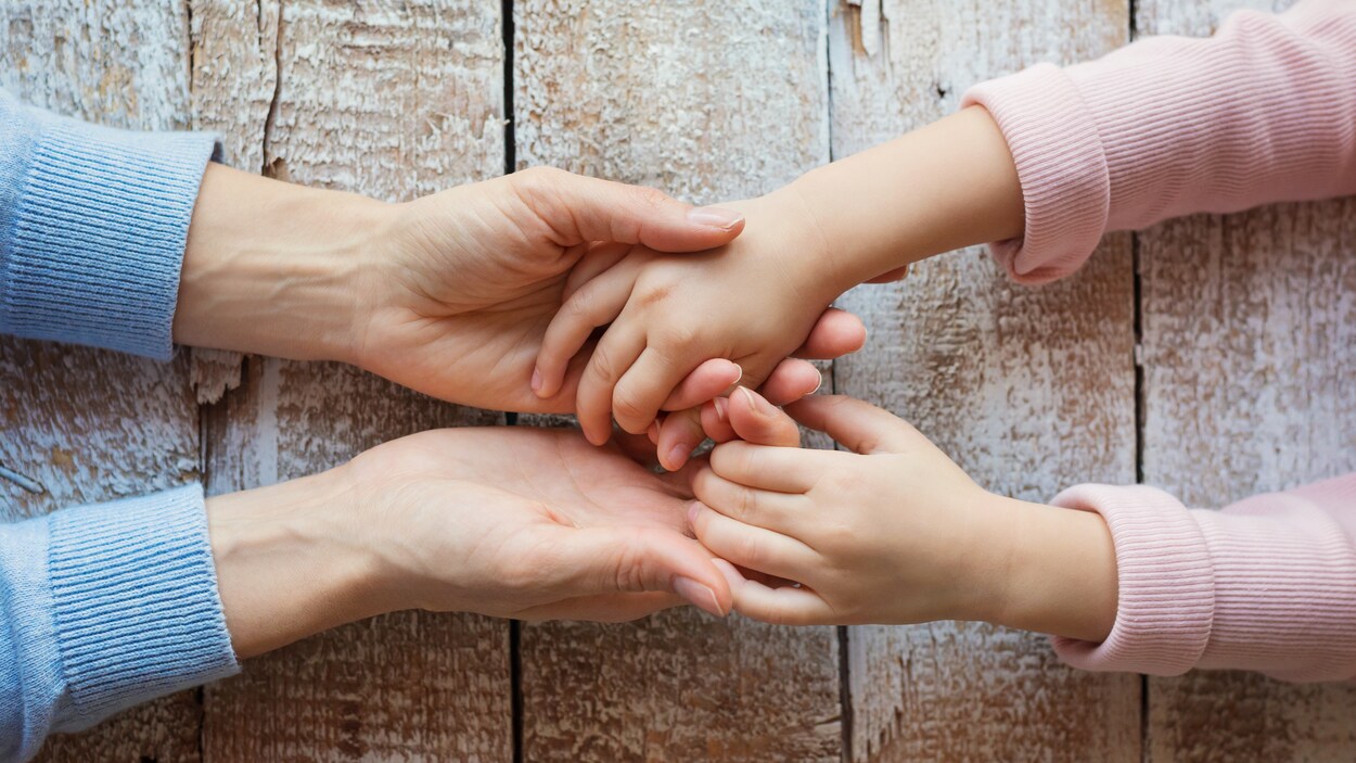 Sur fond de planches de bois, un parent tient les mains de son enfant.