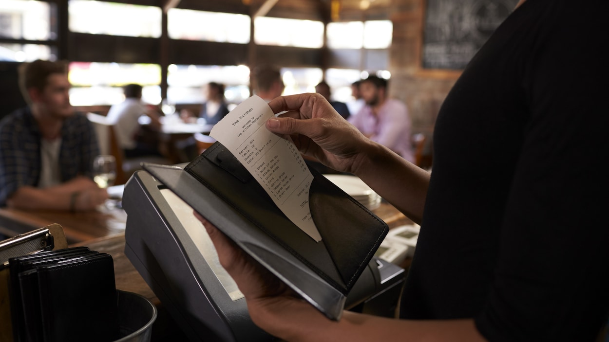 Une serveuse s'apprête à donner l'addition à un consommateur.