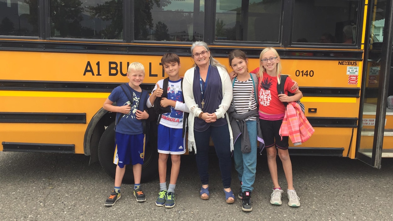 La directrice de l'école Collines D'or, à Kamloops, Lise Bilodeau, et ses élèves posent debout devant un bus scolaire jaune.
