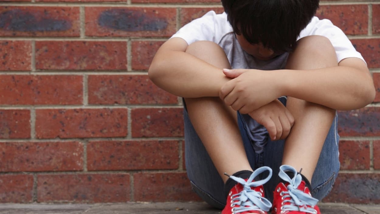 Un enfant assis contre un mur, l'air triste.