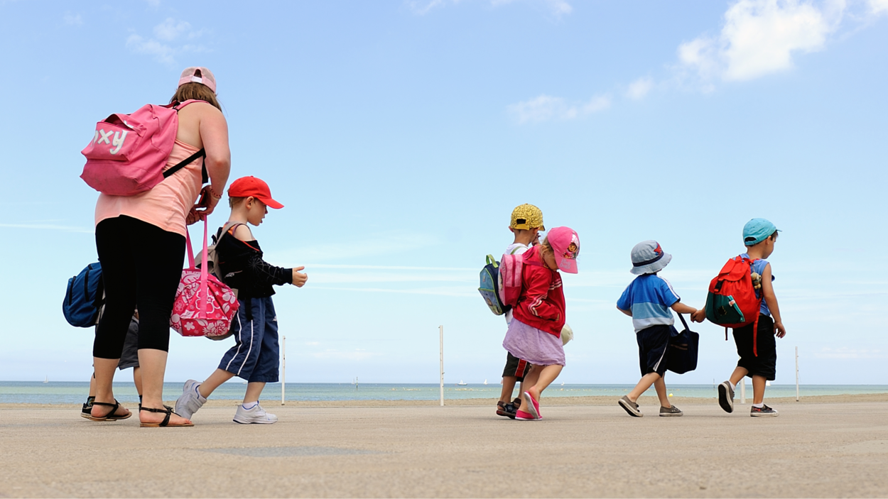 Une femme et des enfants se baladent près de l'océan.