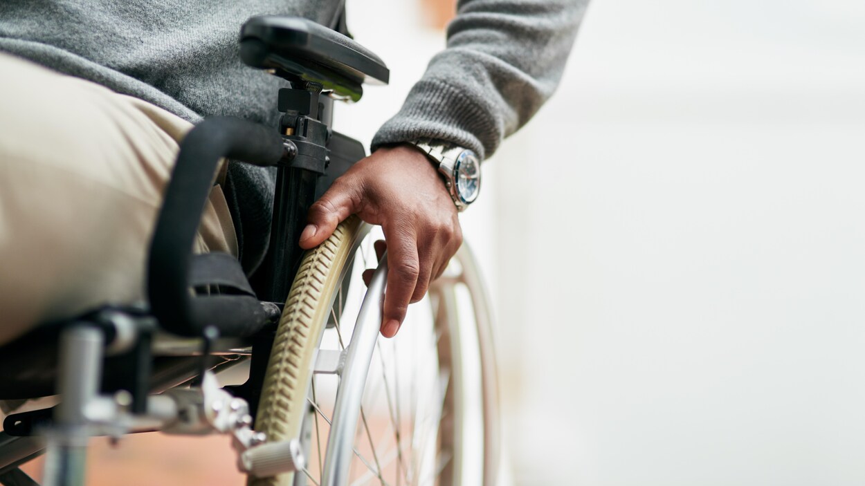 Un homme en fauteuil roulant a une main posée sur une roue.