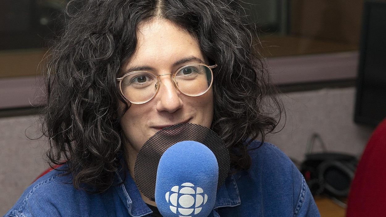 Dans un studio, une femme sourit légèrement devant un micro.