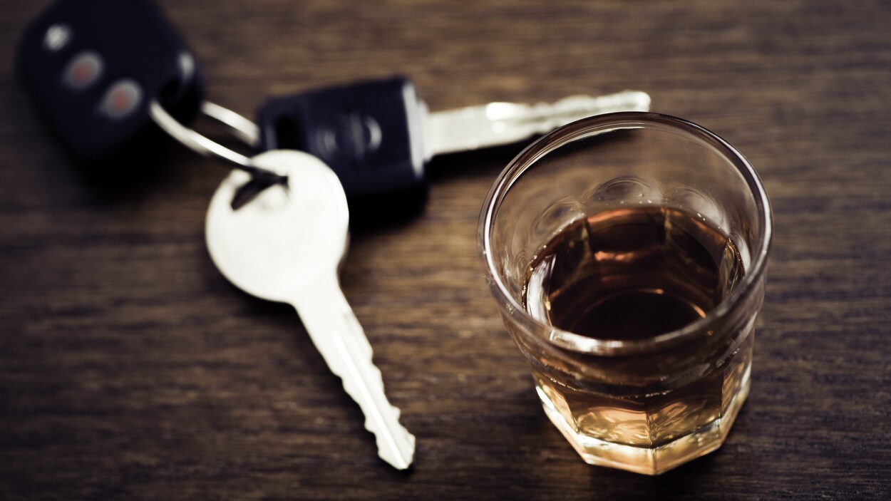 Des clés sont sur une table, posées à côté d'un verre de whisky. Des clés sont sur une table, posées à côté d'un verre de whisky.