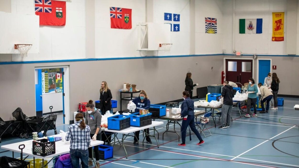 Un gymnase d'une école avec des personnes qui s'occupent d'emballer et de livrer des repas.