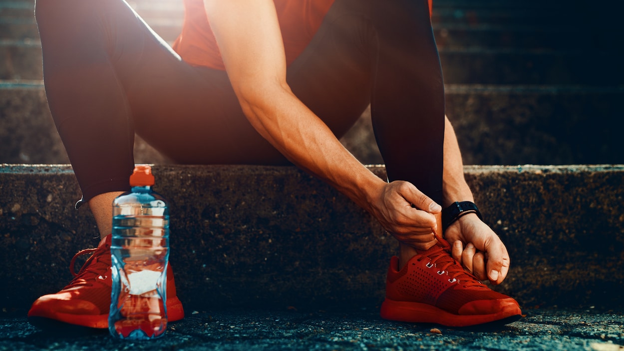 Un homme assis sur des marches à côté d'une bouteille d'eau serre les lacets de ses chaussures de course.