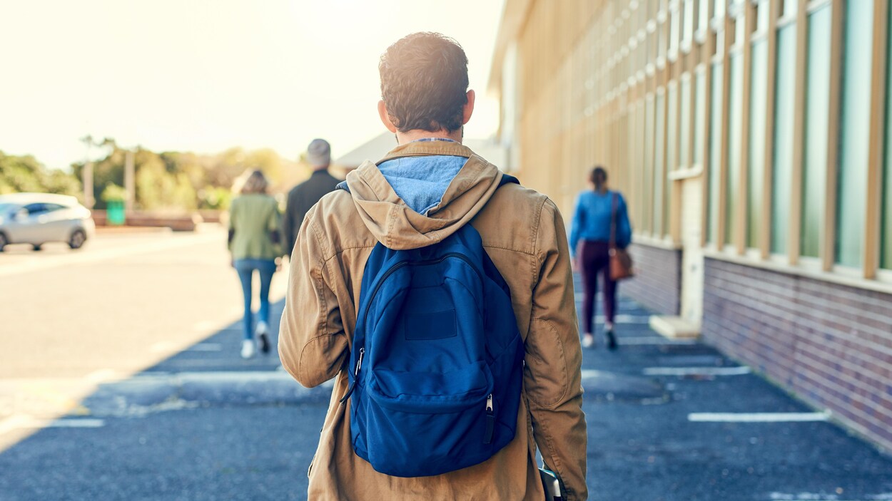 Un homme vu de dos, portant un sac à dos, marchant dans un campus universitaire.