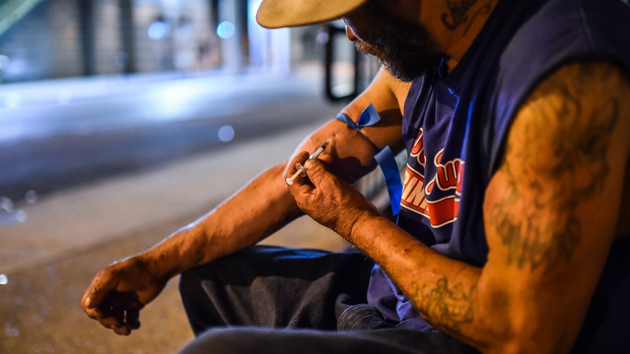 Un homme s'injecte de l'héroïne dans la rue, la nuit.