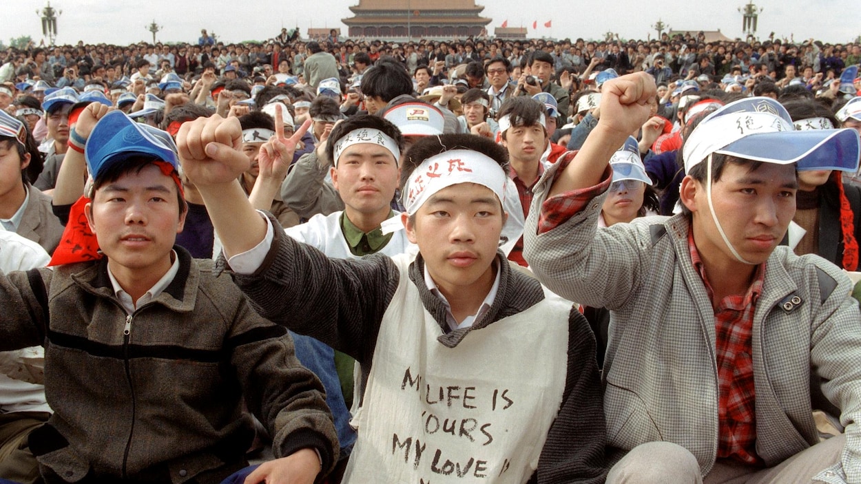 Des jeunes chinois sont assis sur la place Tiananmen en levant le poing en signe de protestation.