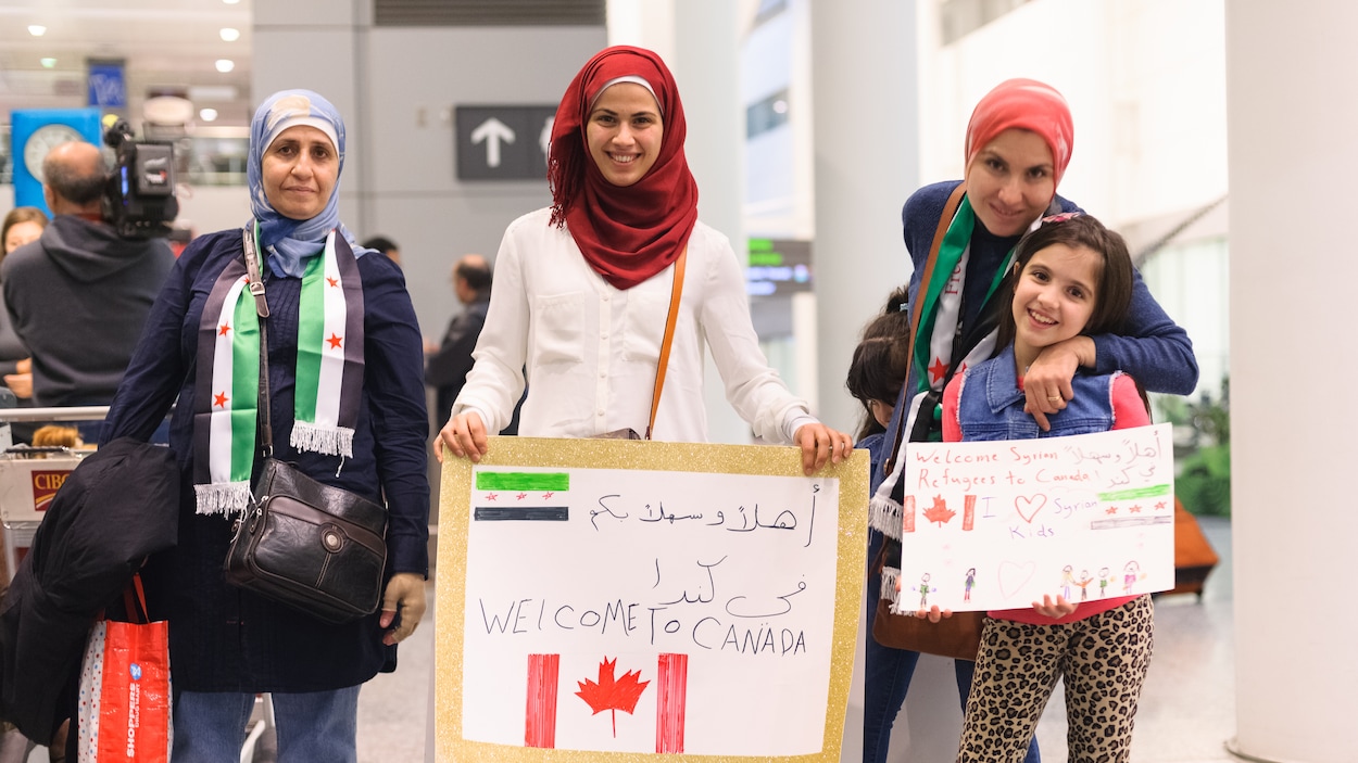 Trois femmes et une jeune fille attentent à l'aéroport avec des pancartes.