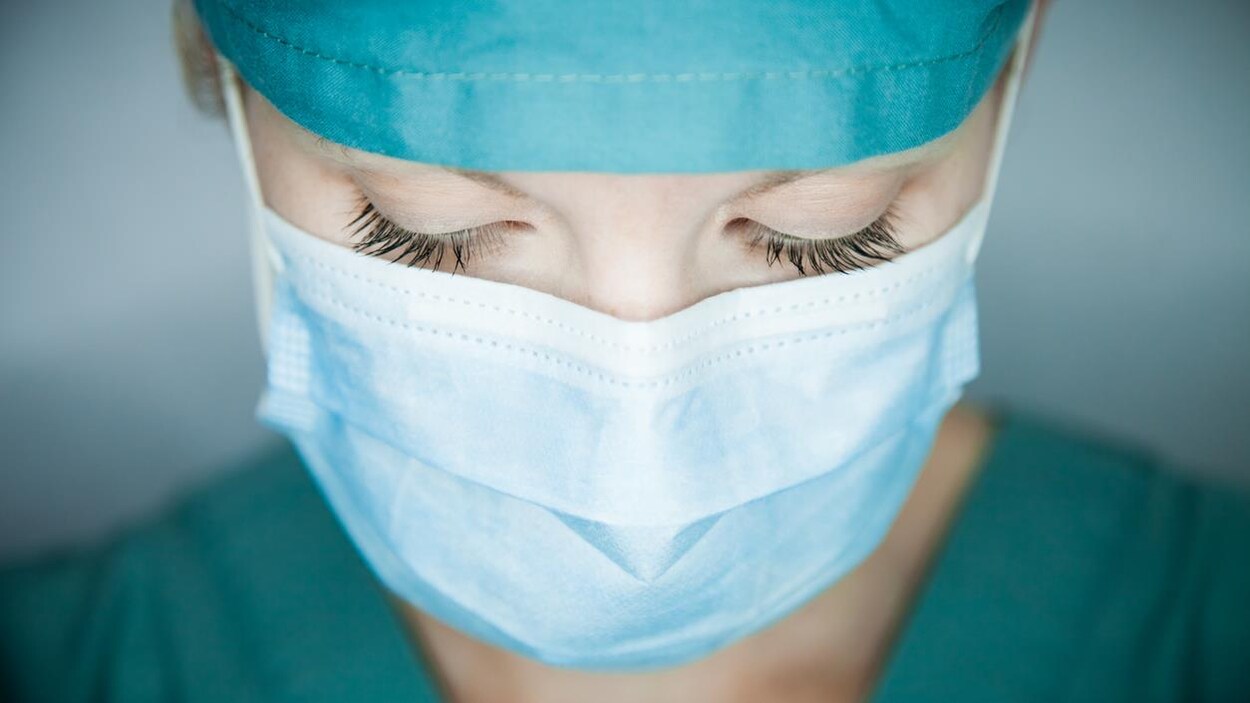 Une femme porte un masque et une tenue de soignant.