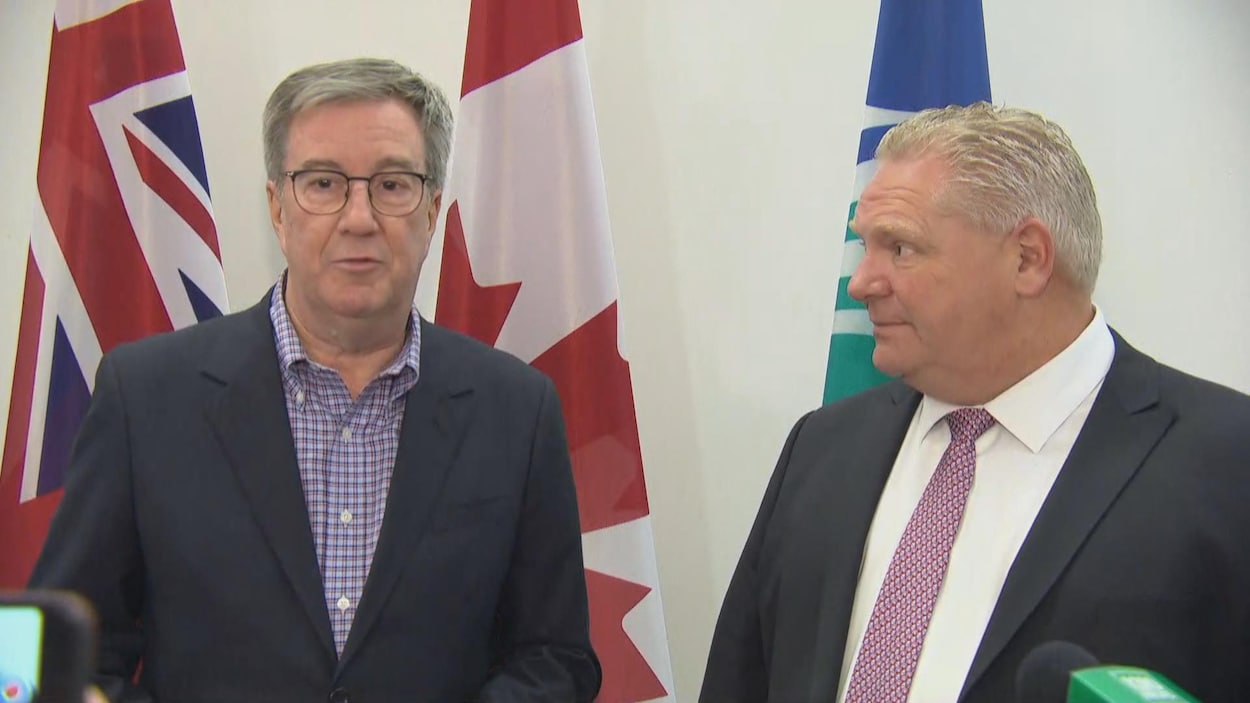 Jim Watson et Doug Ford s'adressent aux médias devant les drapeaux de l'Ontario, du Canada et de la Ville d'Ottawa.