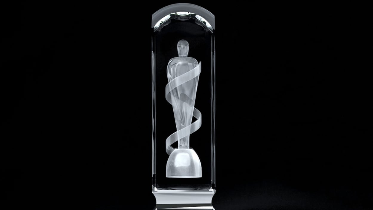 Une statuette rectangulaire en cristal est présentée sur un fond noir. À l'intérieur de ce cristal est gravé au laser le corps d'une personne qui se tient debout et qui est enveloppée d'un ruban.