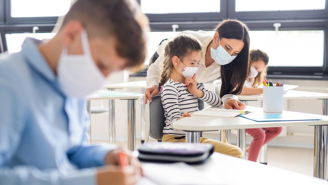 Un groupe de jeunes élèves portant un masque et assis en classe.