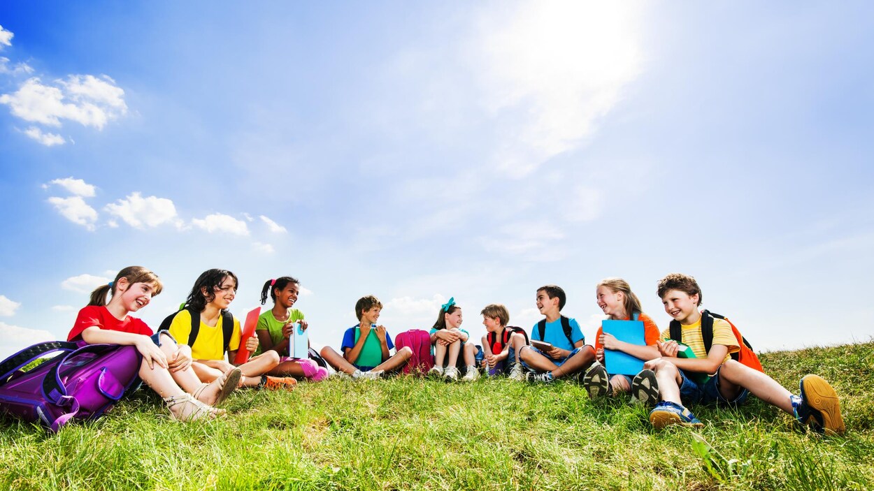 Un groupe de jeunes élèves assis dans l'herbe avec leur sac à dos et leurs livres.