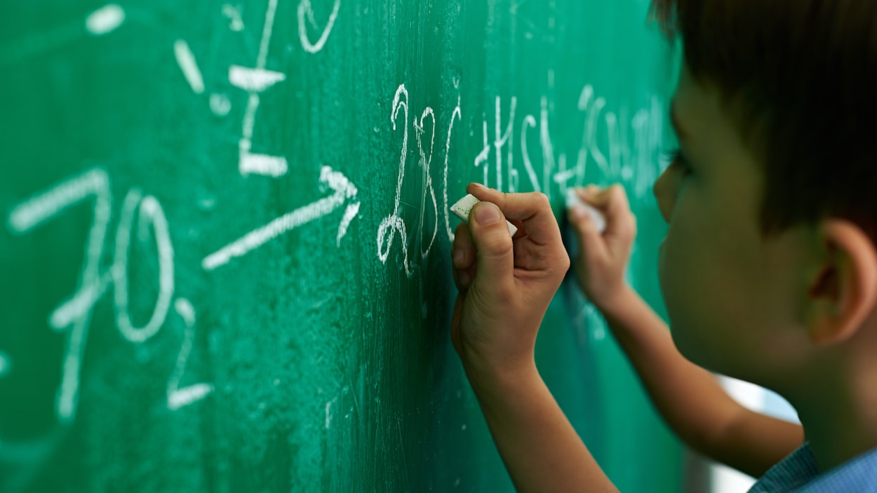 Un jeune homme écrit une formule mathématique au tableau, en classe. Un jeune homme écrit une formule mathématique au tableau, en classe.