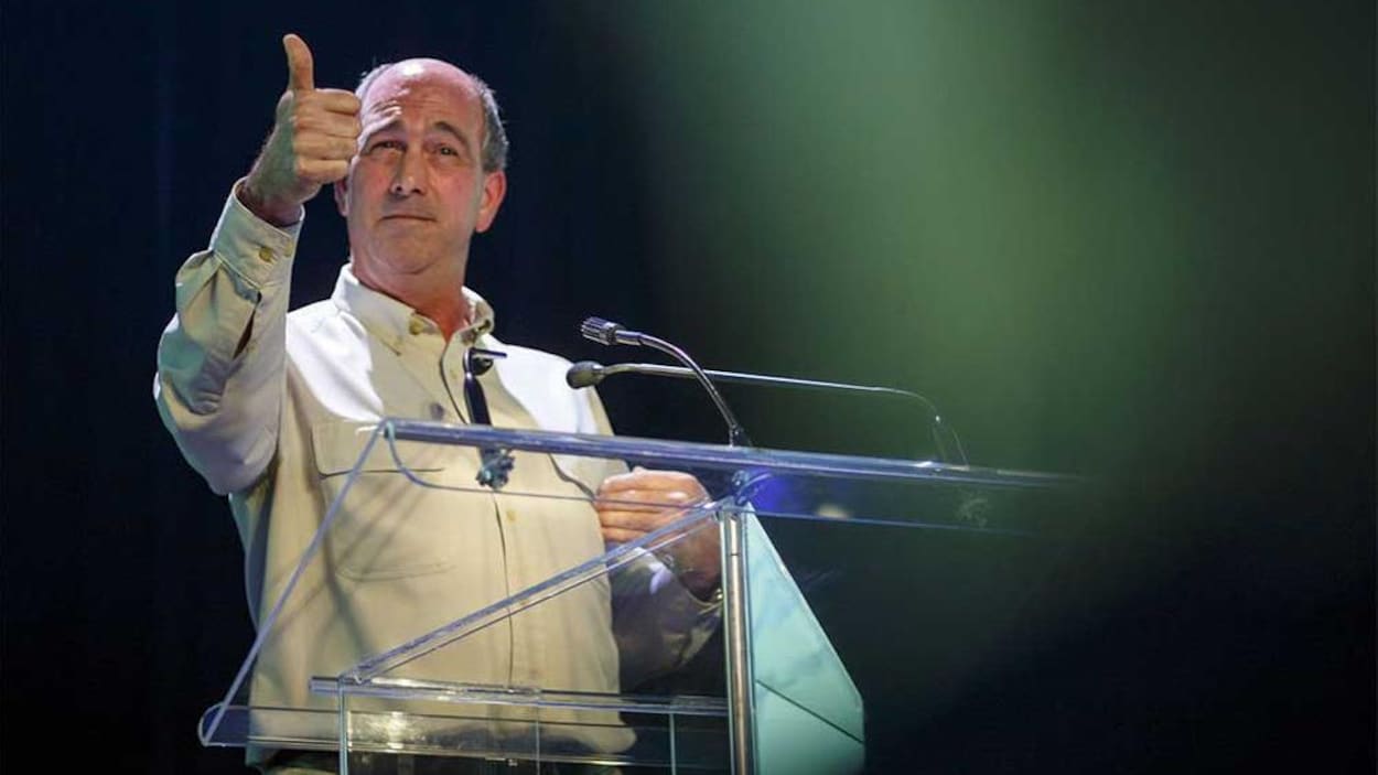 Un homme se tient devant un podium sur une scène. Il donne une conférence.