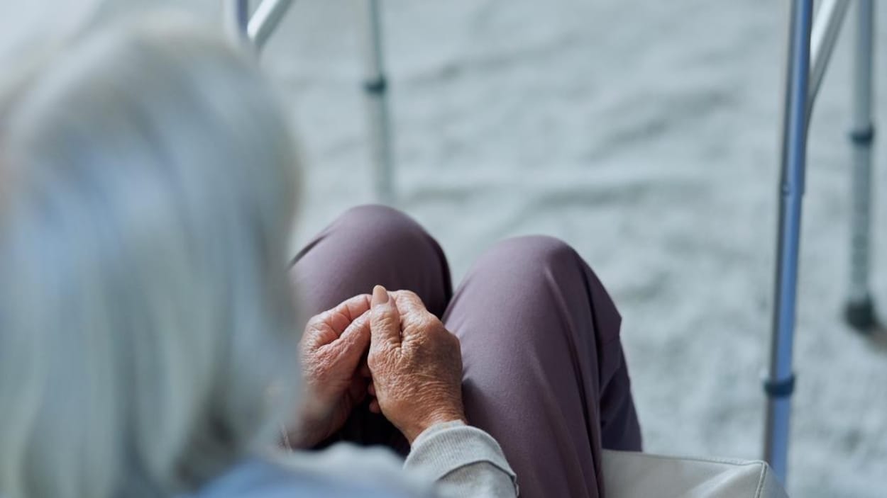 Une femme âgée assise à côté de son déambulateur.