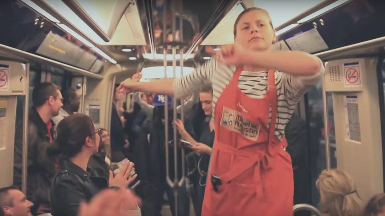 Une femme portant un tablier debout sur un banc dans un métro bondé de monde.