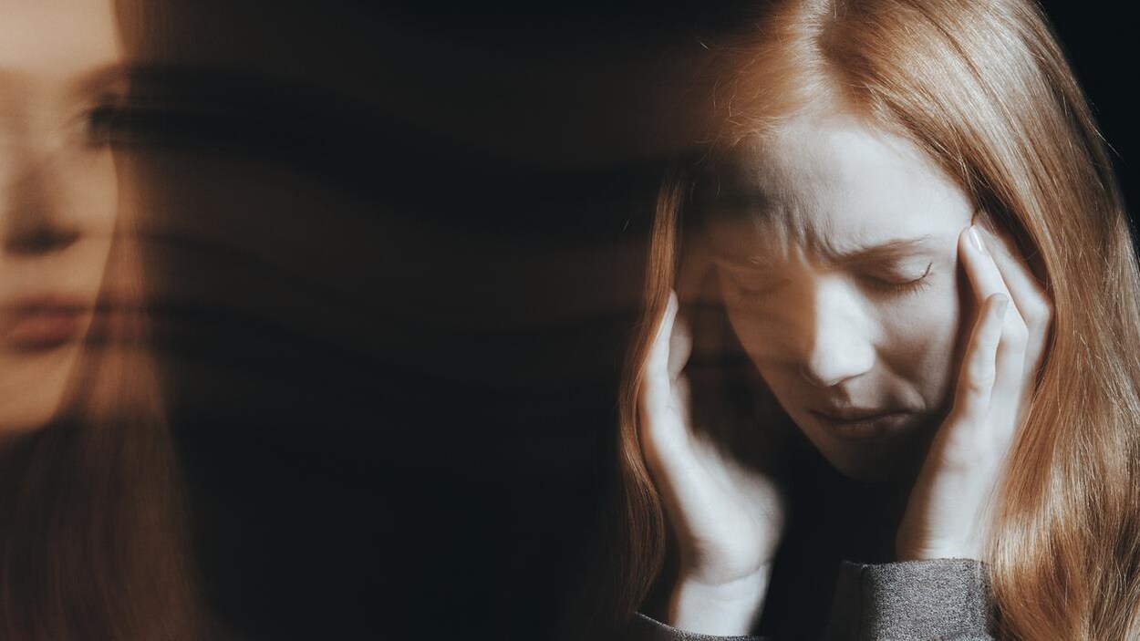 Image floutée d'une femme se tenant la tête et grimaçant de douleur.