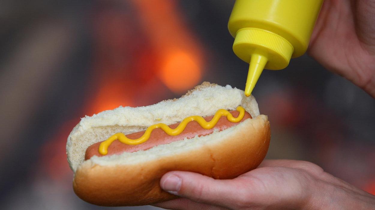 Une personne met de la moutarde dans un hot-dog.