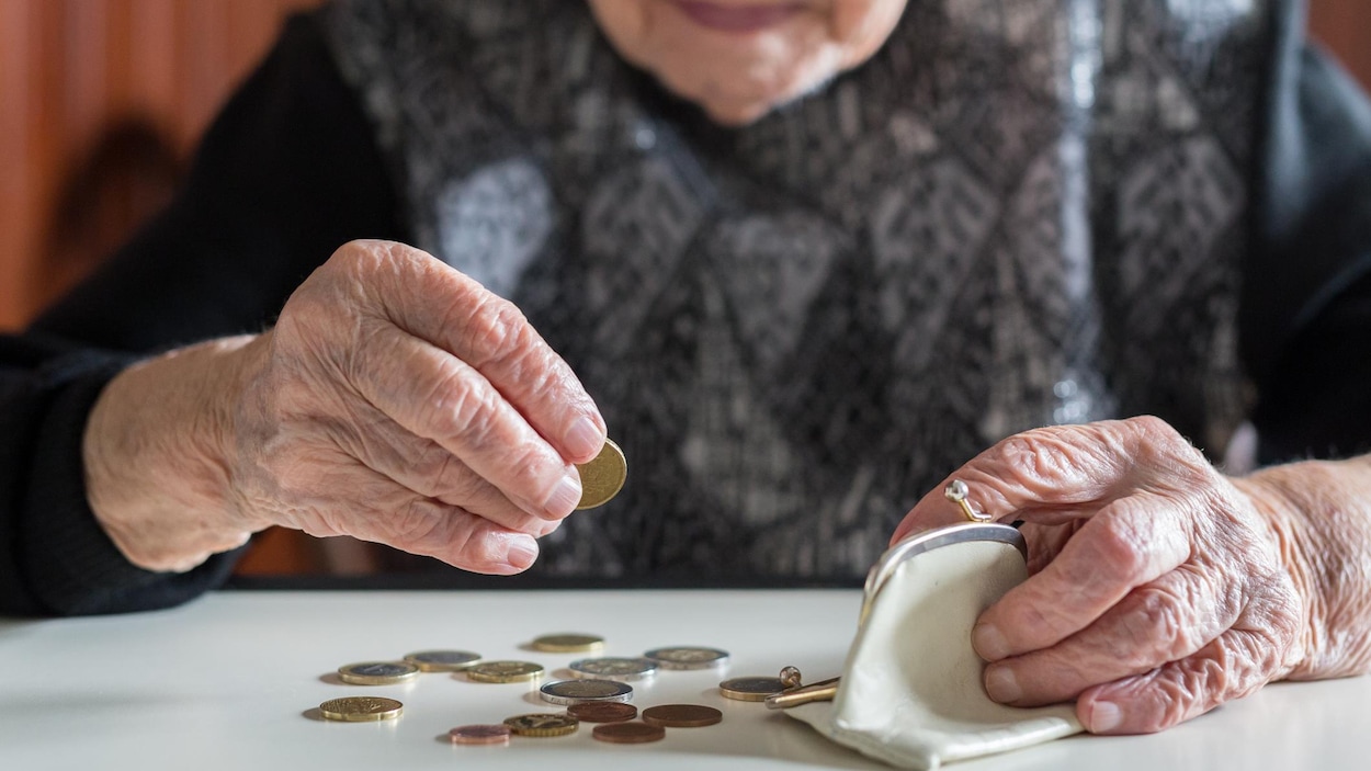 Une dame âgée compte ses sous, posés sur une table devant elle.