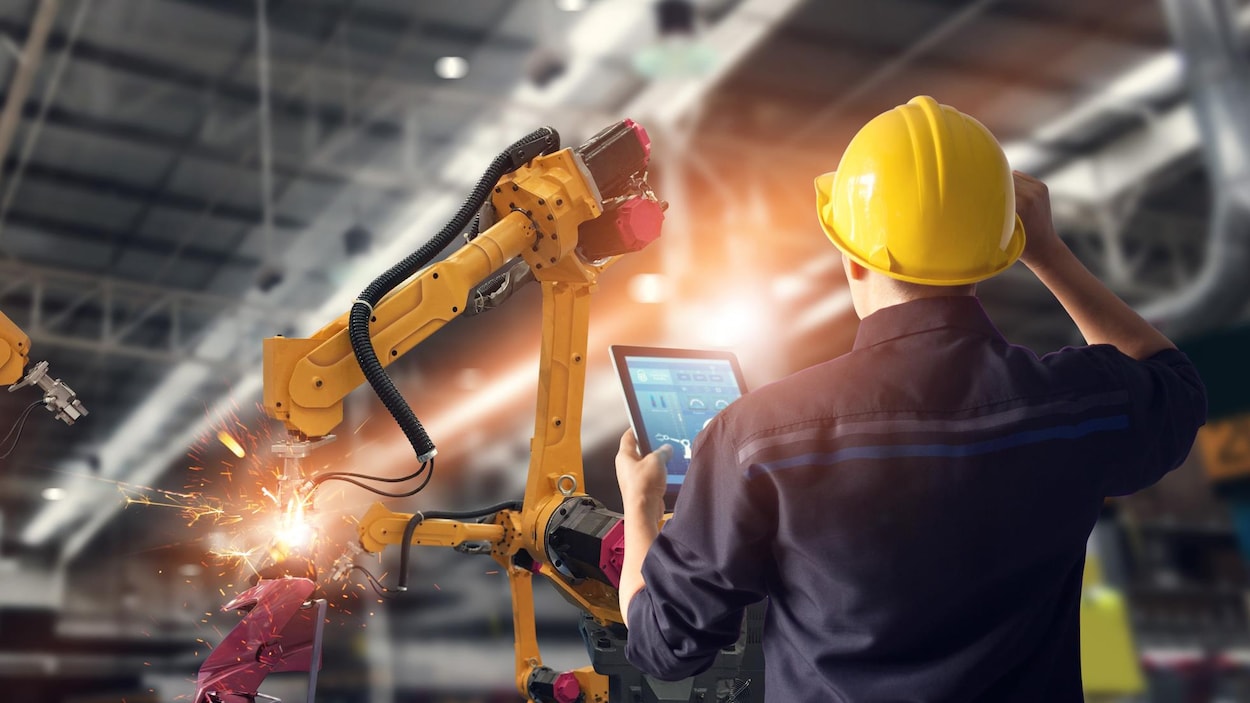 Une tâche est effectuée par un robot dans une usine, sous le regard d'un employé.