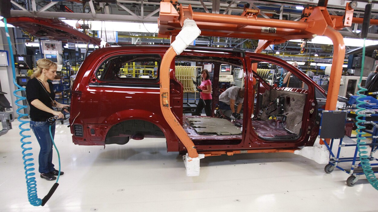 Le châssis d'une voiture en construction avec trois personnes qui installent des pièces dans l'usine Fiat-Chrysler de Windsor.
